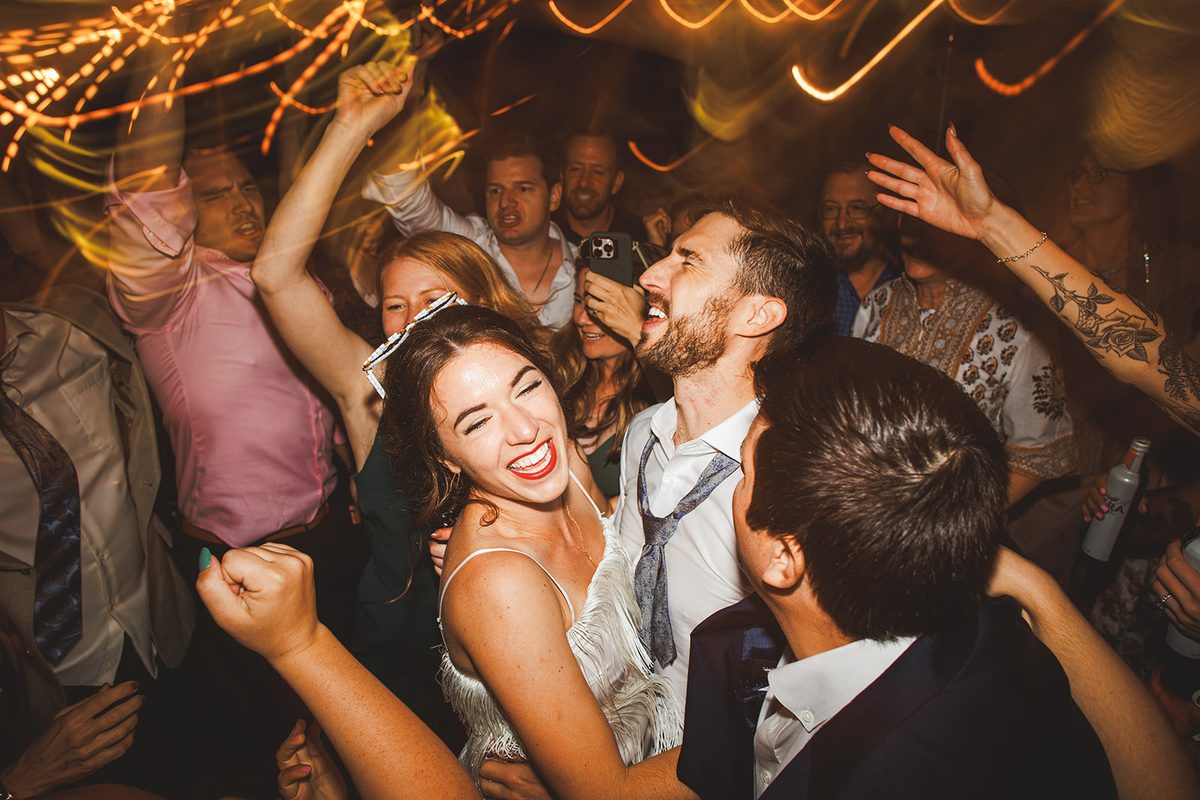 Andrea beaming with her sunglasses pushed up in her hair while Patrick sings beside her, both of them buried in a cheering crowd under ribbons of warm light