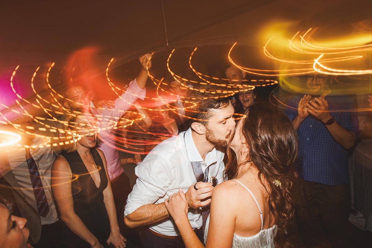 Andrea and Patrick kissing in the middle of the dance floor, her hair swinging and long ribbons of warm light curling around them as guests cheer and clap