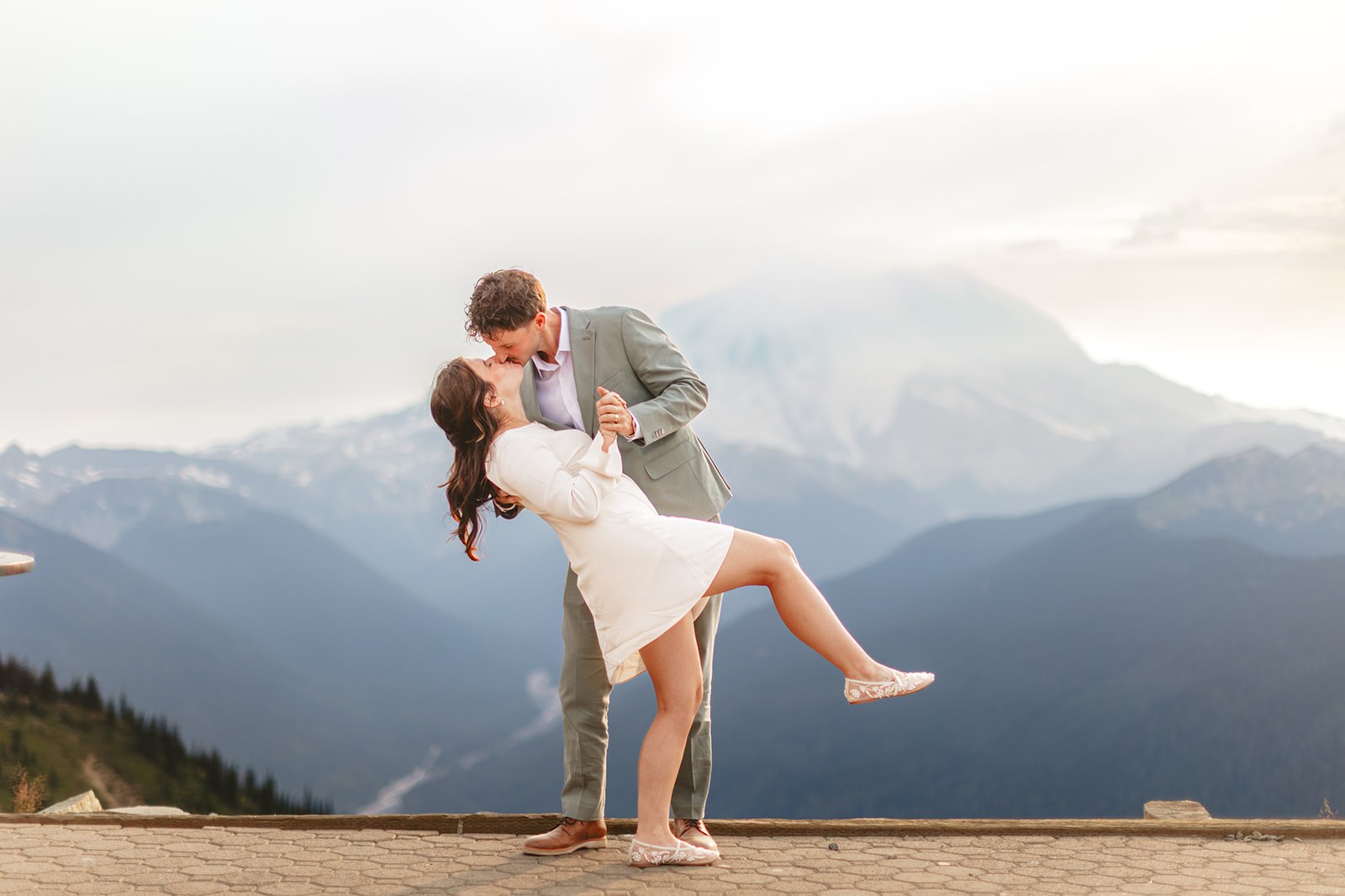 Michaela and AJ joining hands in front of their officiant on the stone terrace at Emmons Vista, their guests standing in a half circle with their backs to the camera and the glaciers of Mount Rainier filling the view behind