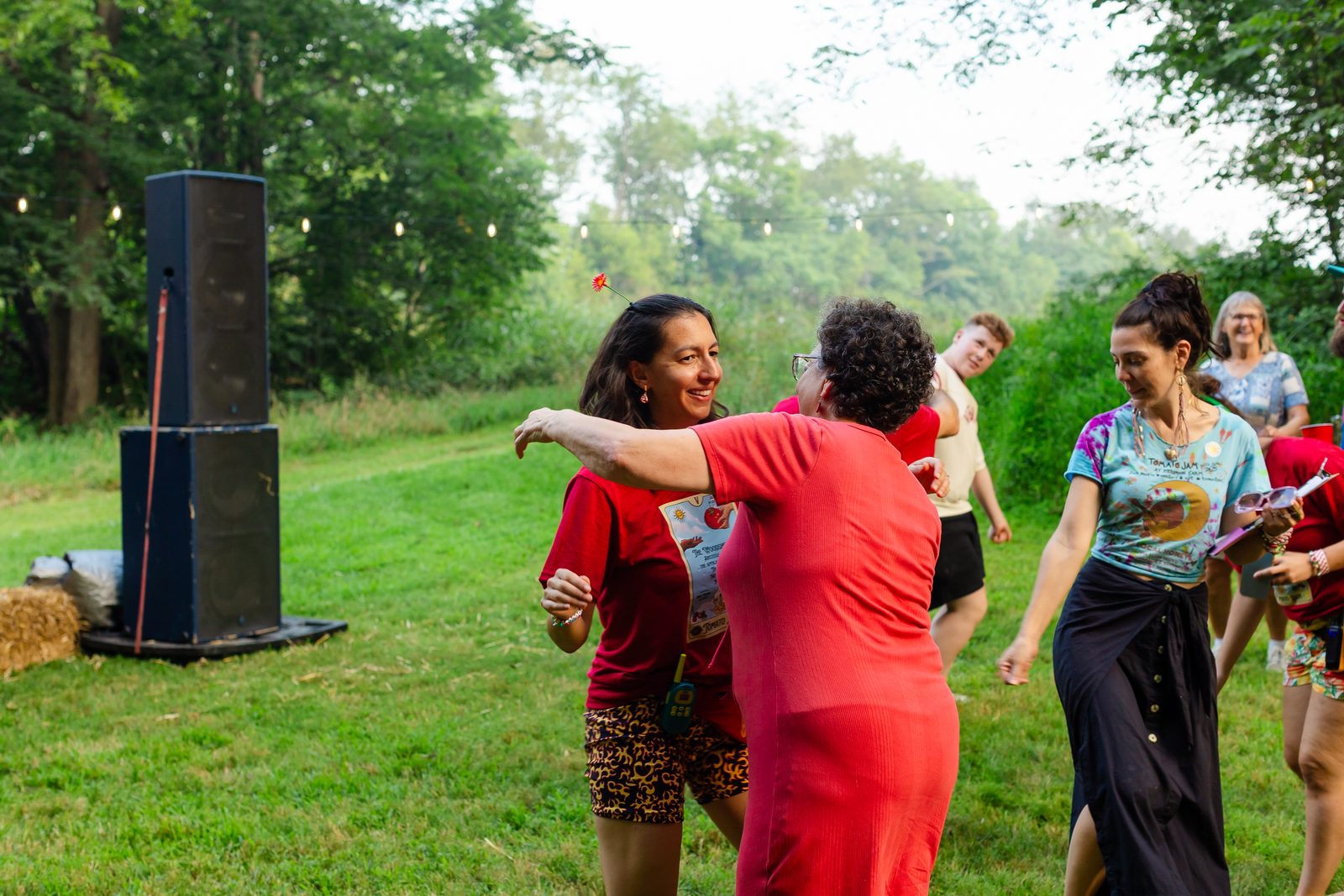 Two women grinning in a hug mid-dance in front of the Tomato Jam stage in warm evening light