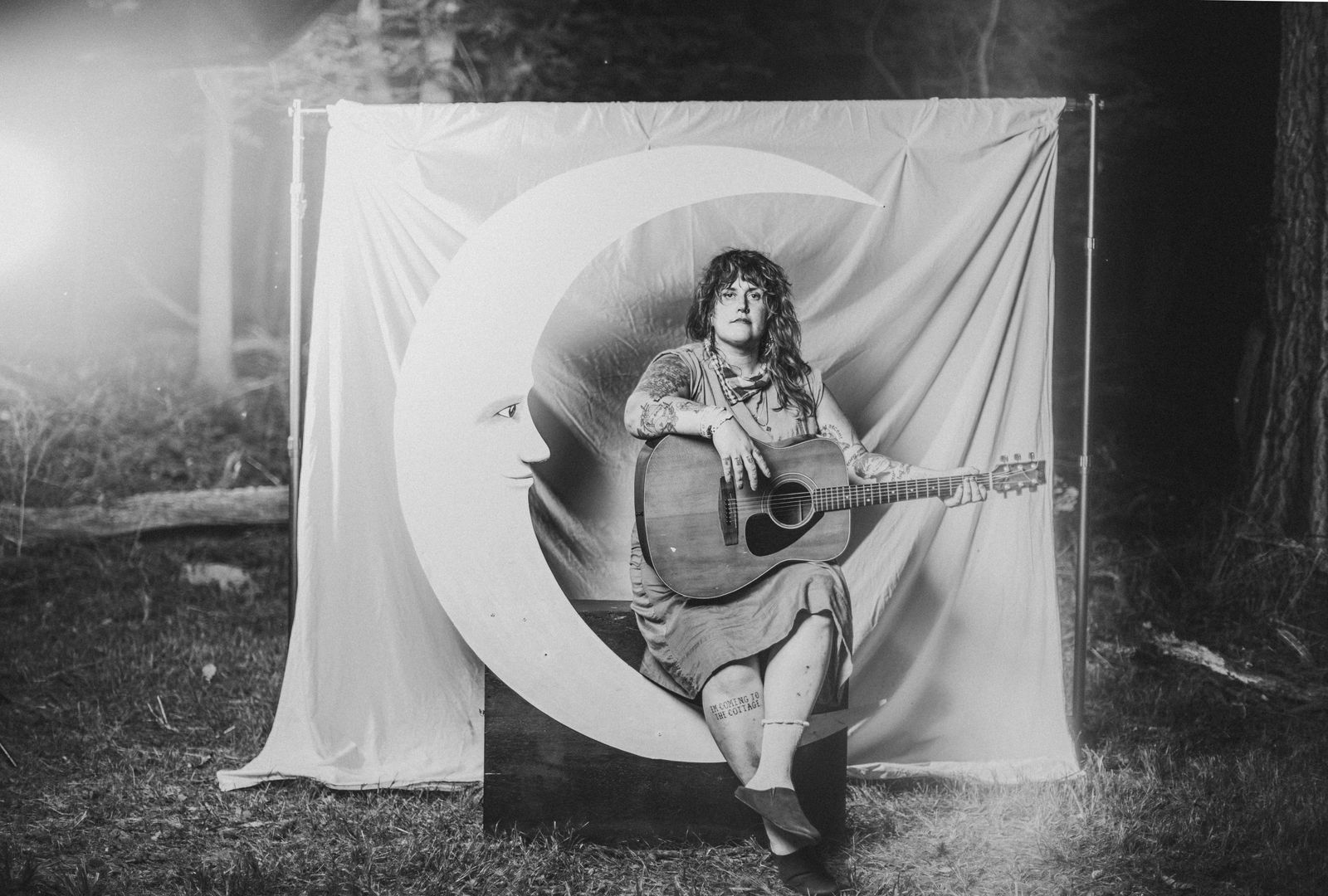 A musician seated in the curve of the crescent moon with an acoustic guitar, in black and white