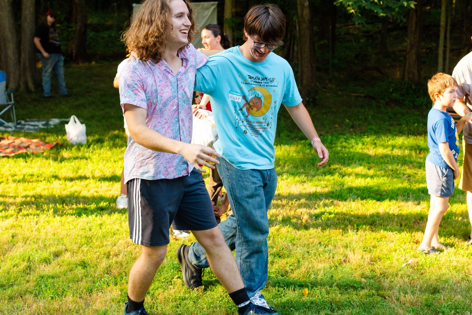 Two teenagers laughing as they walk arm in arm across the sunlit grass at Tomato Jam
