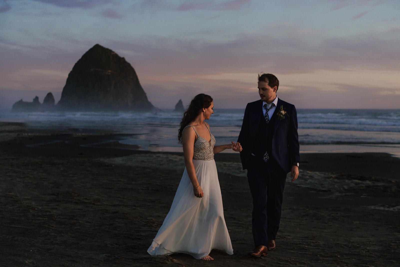 The couple walking the sand at dusk, Haystack Rock behind them at Cannon Beach