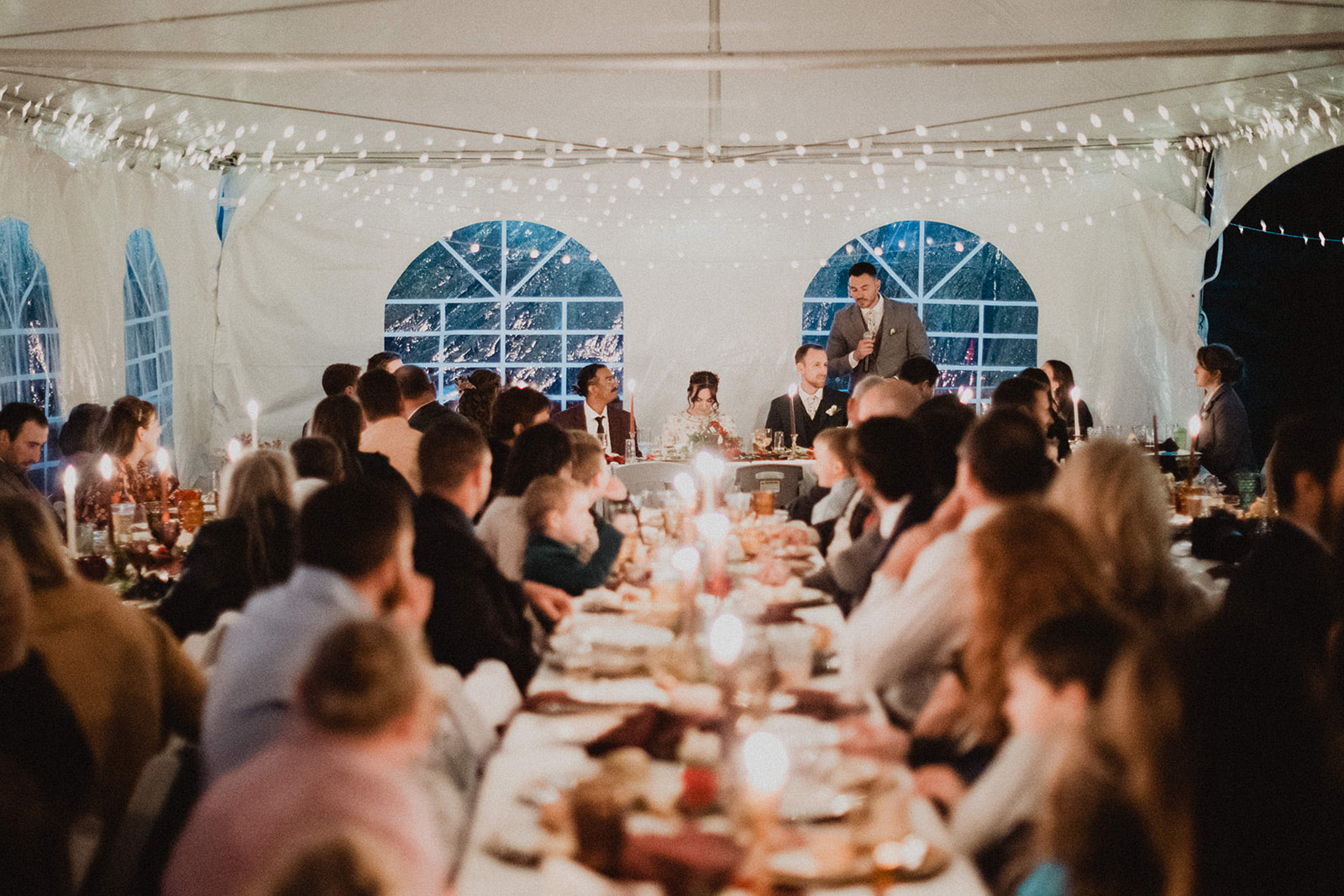Candlelit reception tables full of guests under a tent