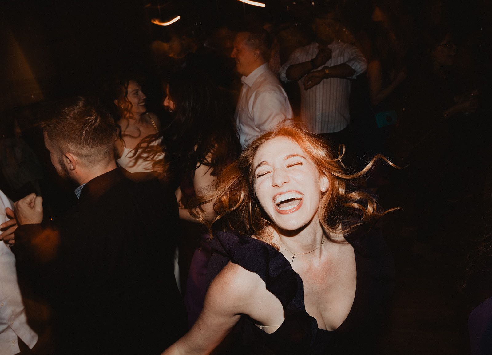 A woman laughs with her head thrown back and her hair flying as other guests dance around her.