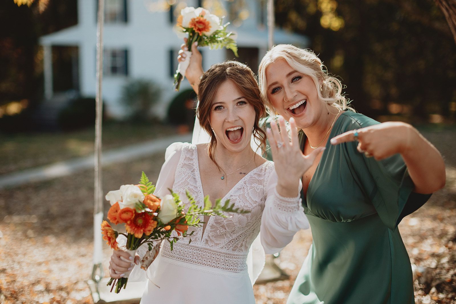 The bride laughs with her mouth wide open as she holds out her ring hand, and a woman in a green dress laughs and points at the ring.