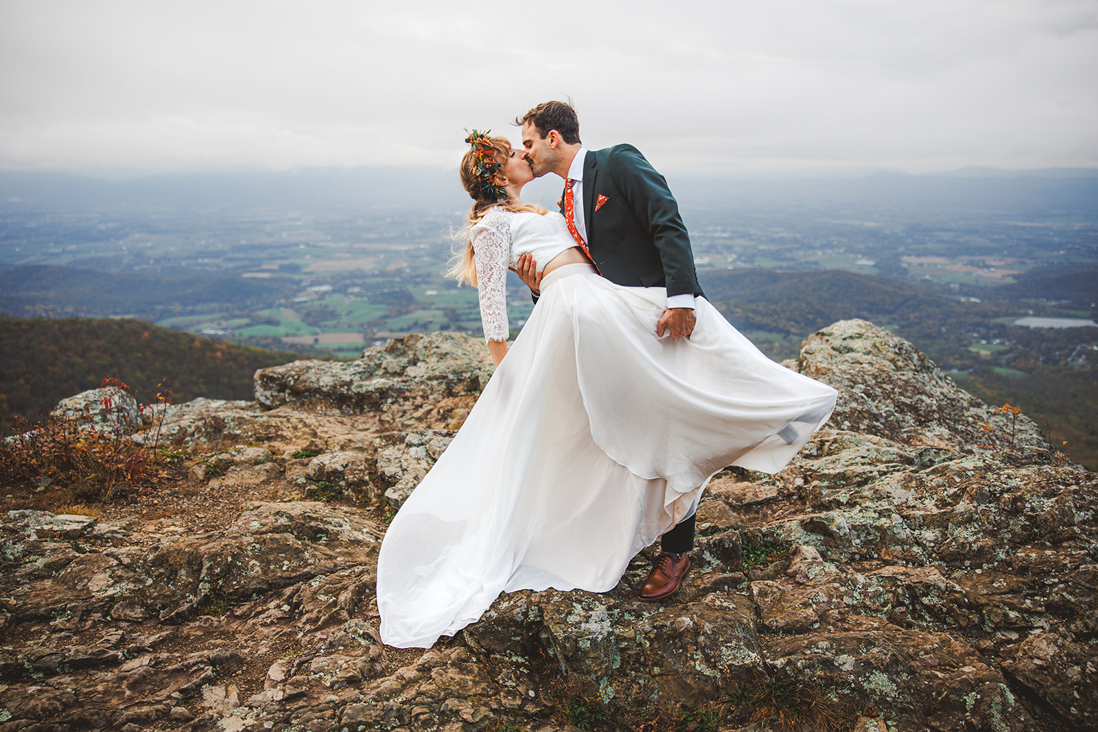 Ryan pulling Sara into a kiss on a rock outcrop above the autumn Shenandoah Valley, her white skirt lifting in the wind
