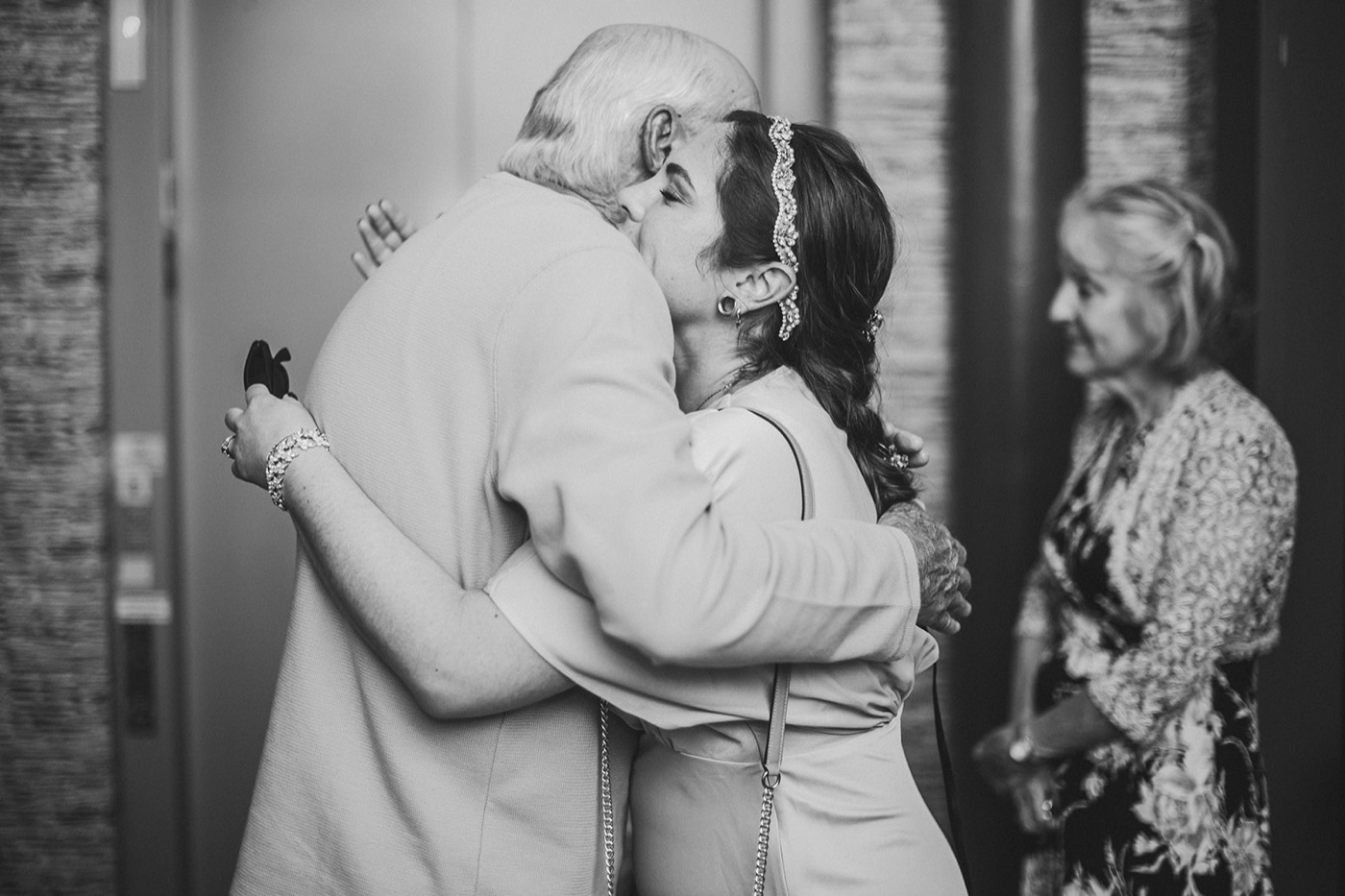 A black and white photograph of an older man holding on to a guest in a long embrace