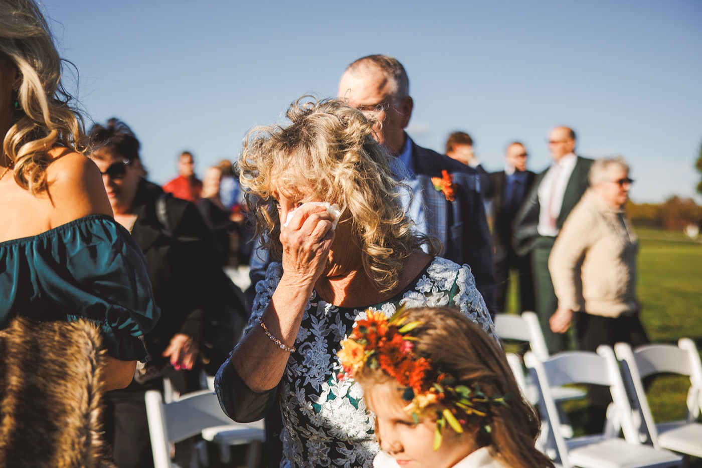 An older guest wiping her eyes during the ceremony while a child in a flower crown stands beside her